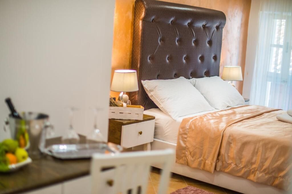 Ein Hotelzimmer mit einer gepolsterten Kopfteil, einem Bett mit weißen Bettwäsche, zwei Nachttischlampen, einem kleinen Tisch mit einer Obstschale und einem weißen Sessel.