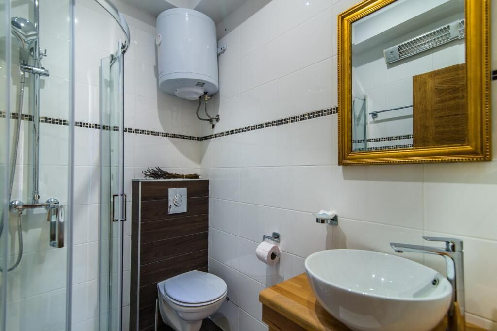 A bathroom with a glass shower enclosure, a toilet, a sink with a wooden countertop, and a mirror with a gold frame.
