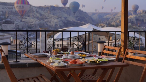 Ein Esstisch mit verschiedenen Gerichten, mit Blick auf eine malerische Aussicht auf Heißluftballons und felsiges Gelände.