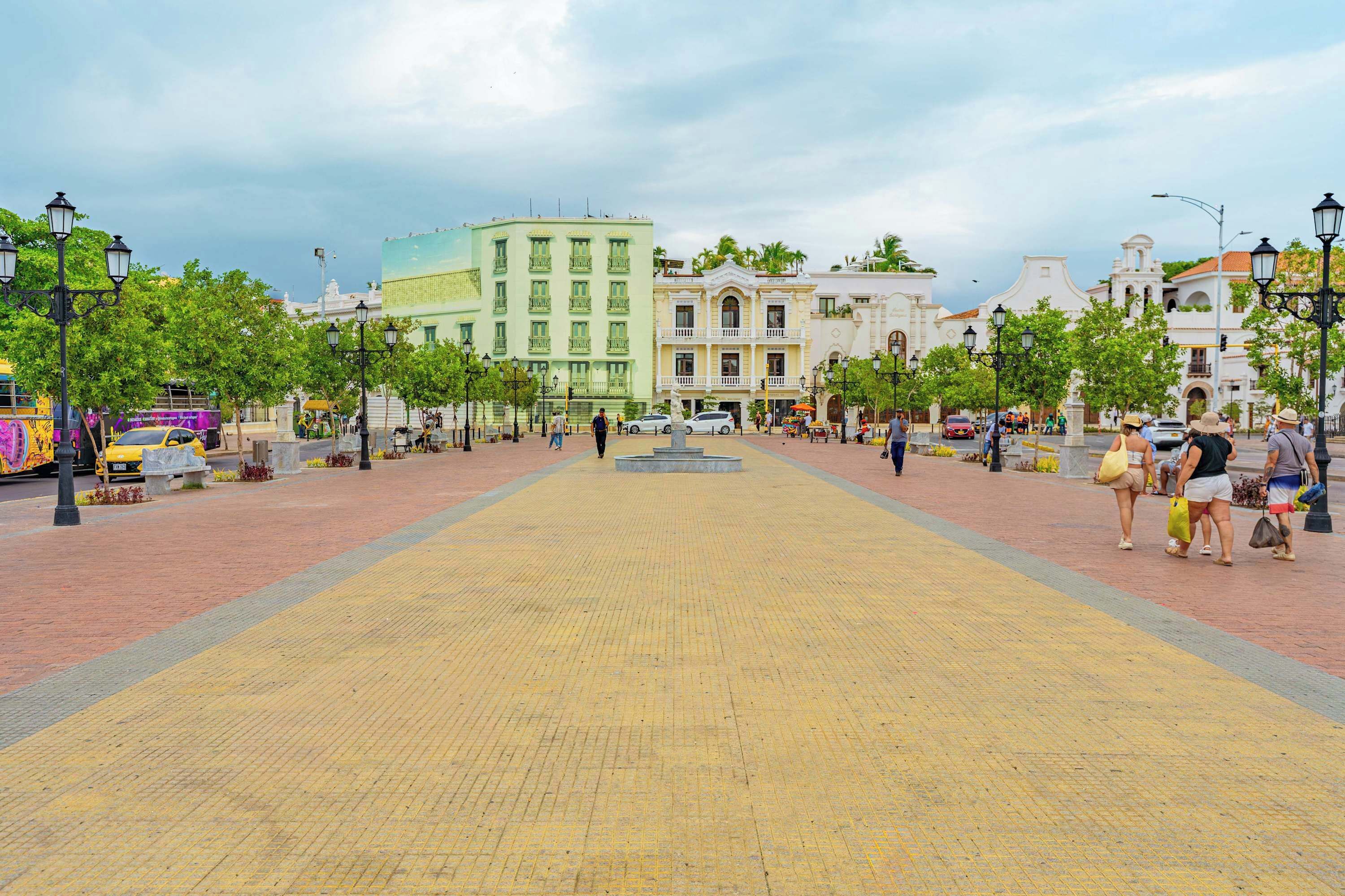 A paved square with buildings, trees, and street lamps.