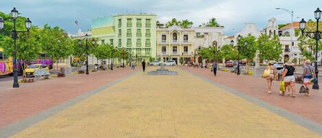 A paved square with buildings, trees, and street lamps.