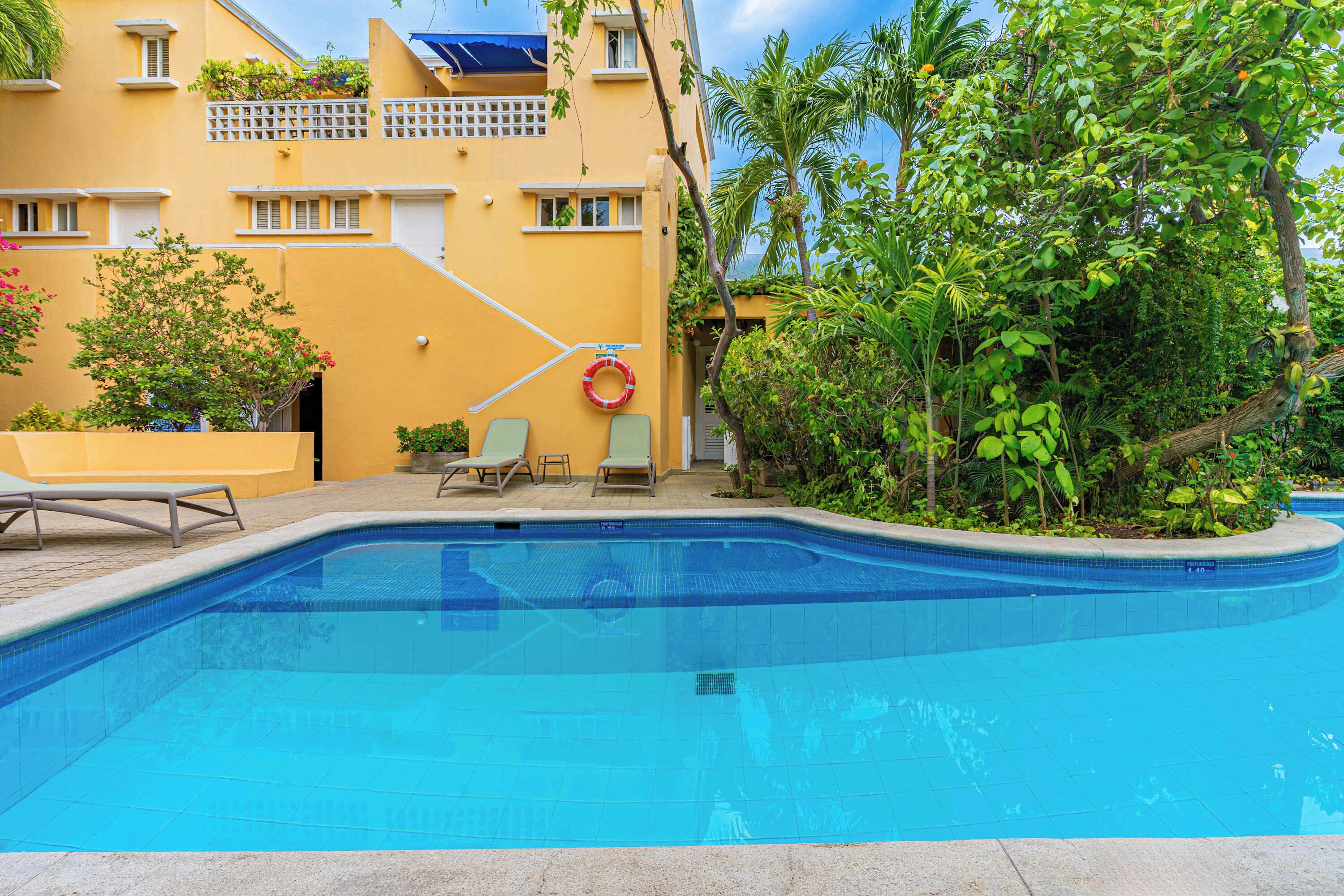 A swimming pool with lounge chairs, a lifebuoy, and a building with balconies and greenery.