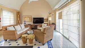Un salon avec un canapé, des fauteuils, un téléviseur et un ventilateur de plafond.