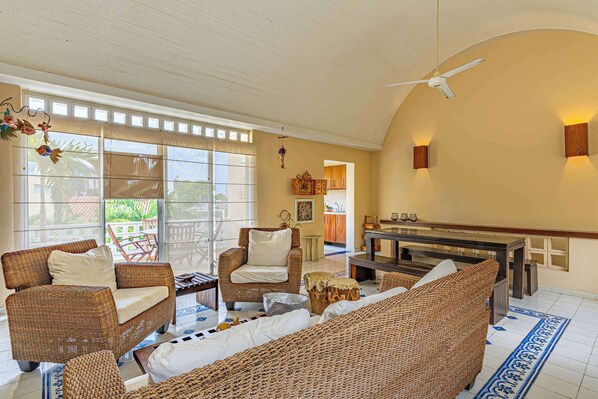 A spacious living area with wicker furniture, a ceiling fan, and a view through large windows. - w* | Charming 2BR w/ Pool & Terrace in Getsemani (Cartagena de Indias)