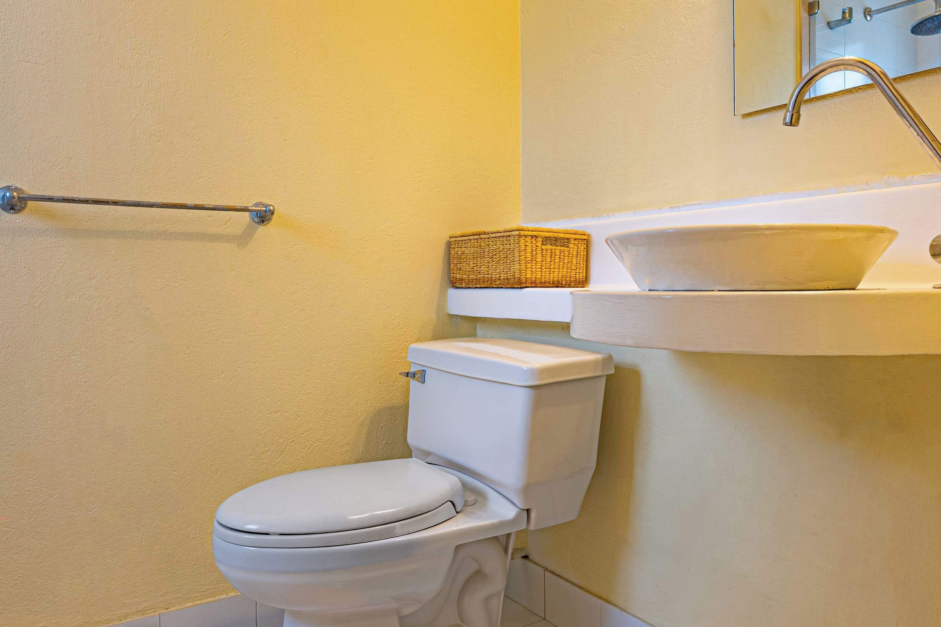 A bathroom with a toilet, a basket on the wall, and a sink with a mirror above it.