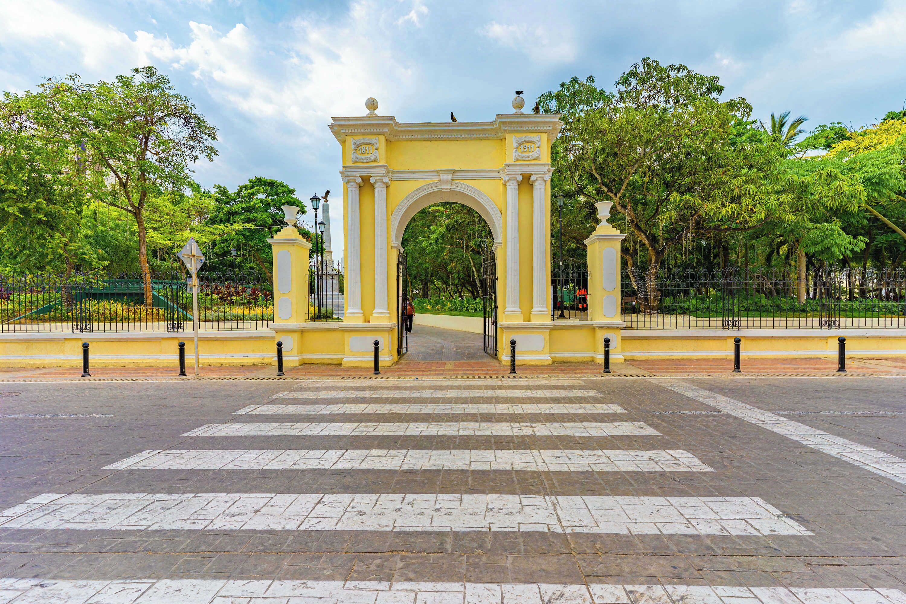 Un arco con un camino despejado que lo atraviesa, rodeado de follaje y una cerca.