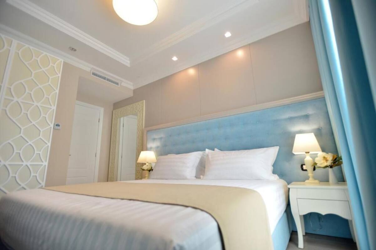A hotel room with a large bed, two bedside tables with lamps, a decorative headboard, and a patterned wall panel.