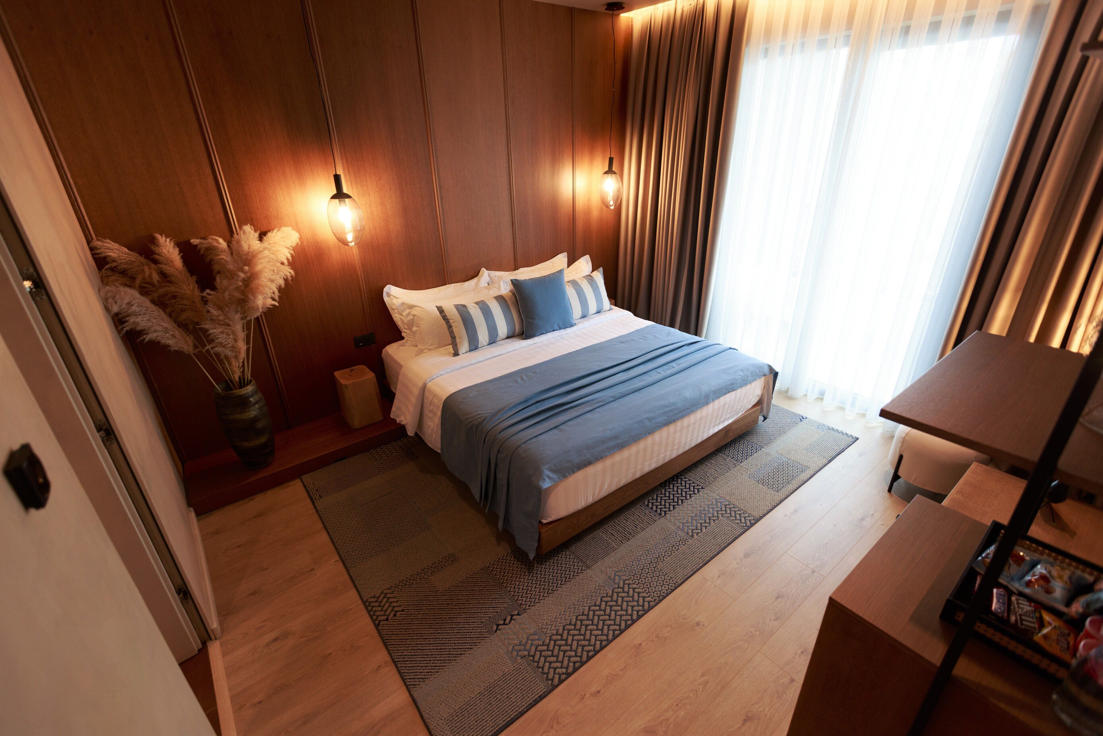 A modern bedroom with a wooden panel wall, a large bed with blue bedding, a bedside table, and a nightstand.