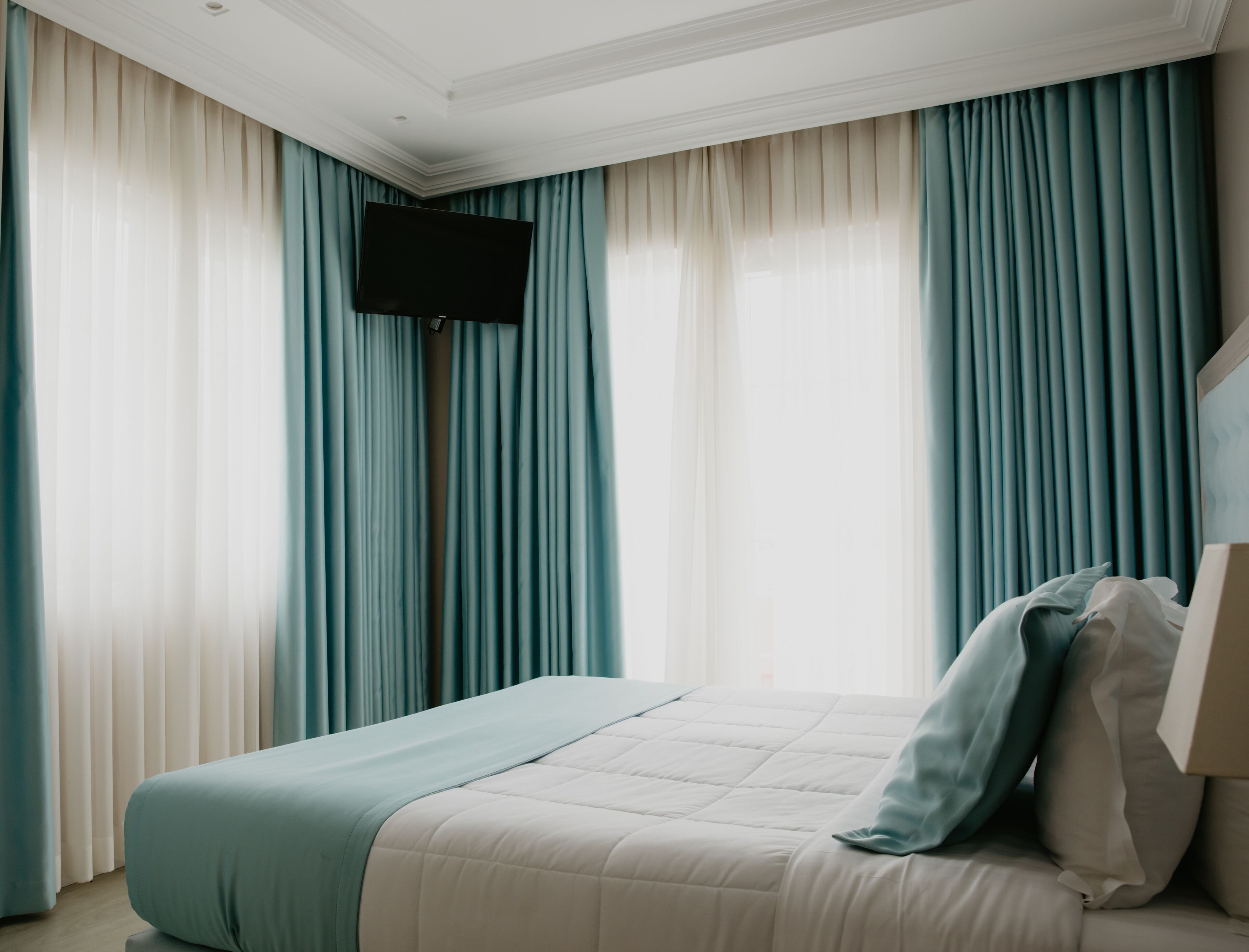 Un dormitorio con cama, un televisor de pantalla plana montado en la pared y cortinas.