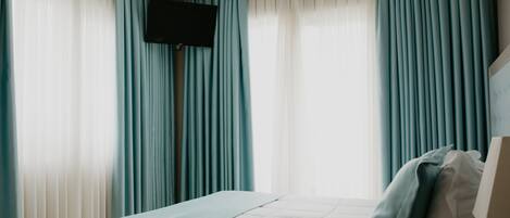 A bedroom with a bed, a flat-screen TV mounted on the wall, and curtains.