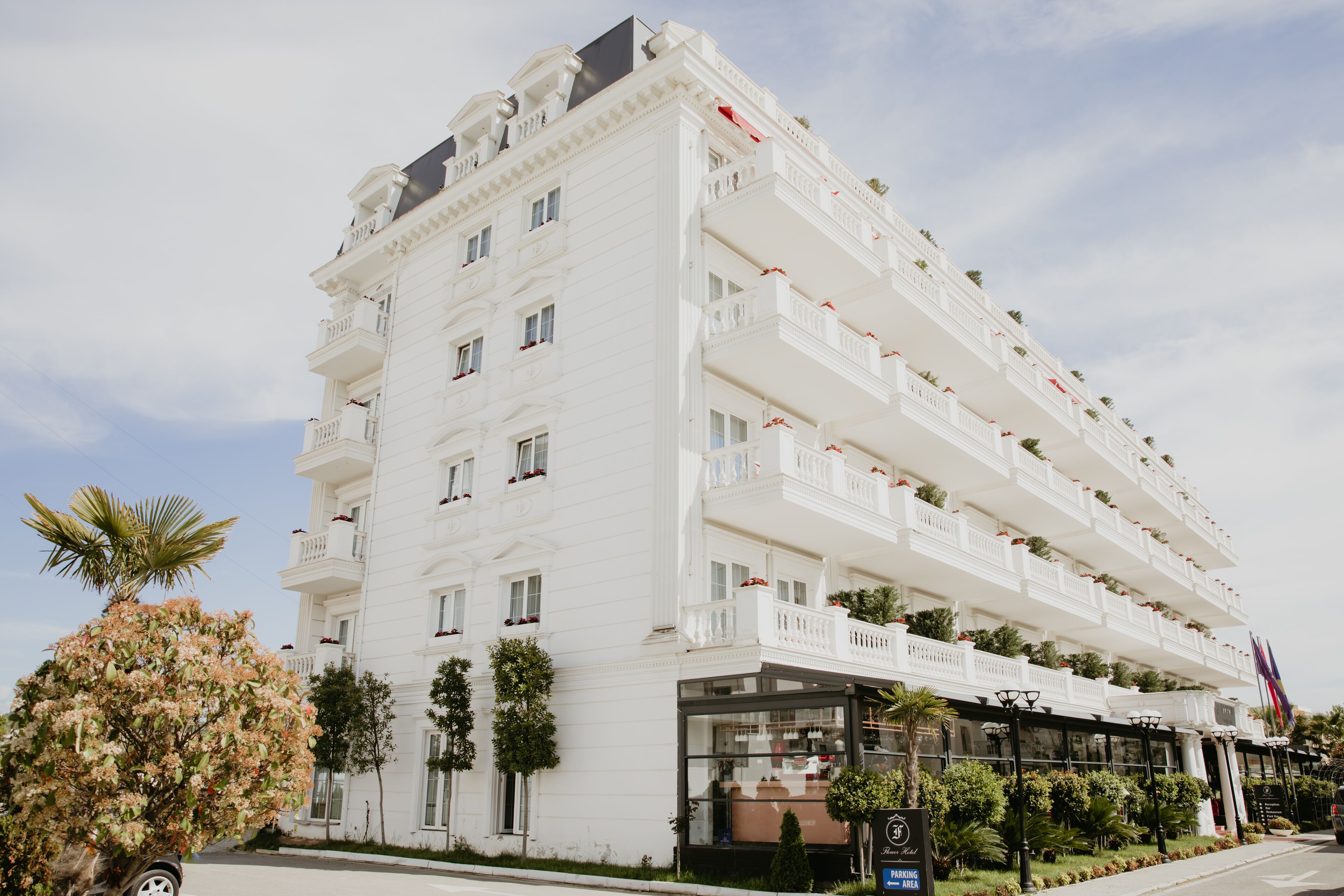 Un hotel de varios pisos con balcones, entrada de vidrio y señal de estacionamiento.
