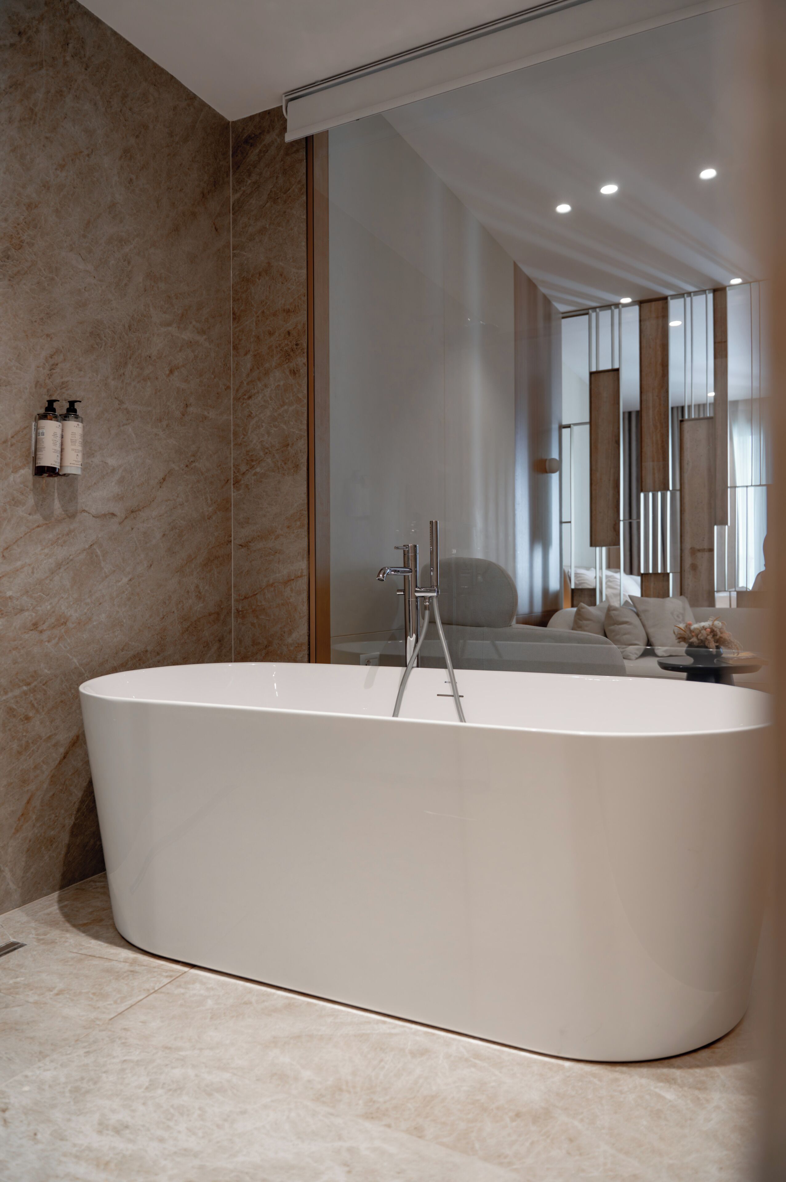 A modern bathroom with a freestanding bathtub, a large mirror, and a seating area with a sofa and table.