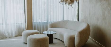 A modern living room with a beige sofa, two ottomans, and a small round table.