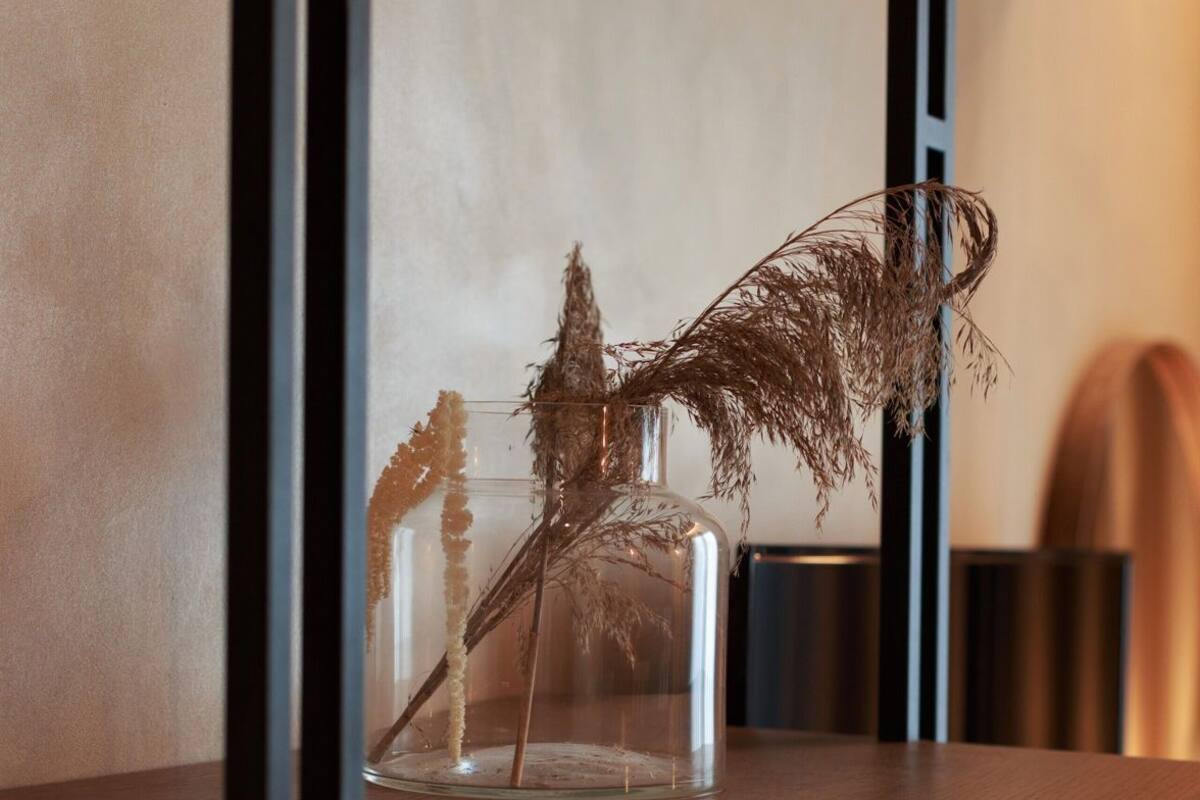 A clear glass vase with dried plants on a wooden shelf.