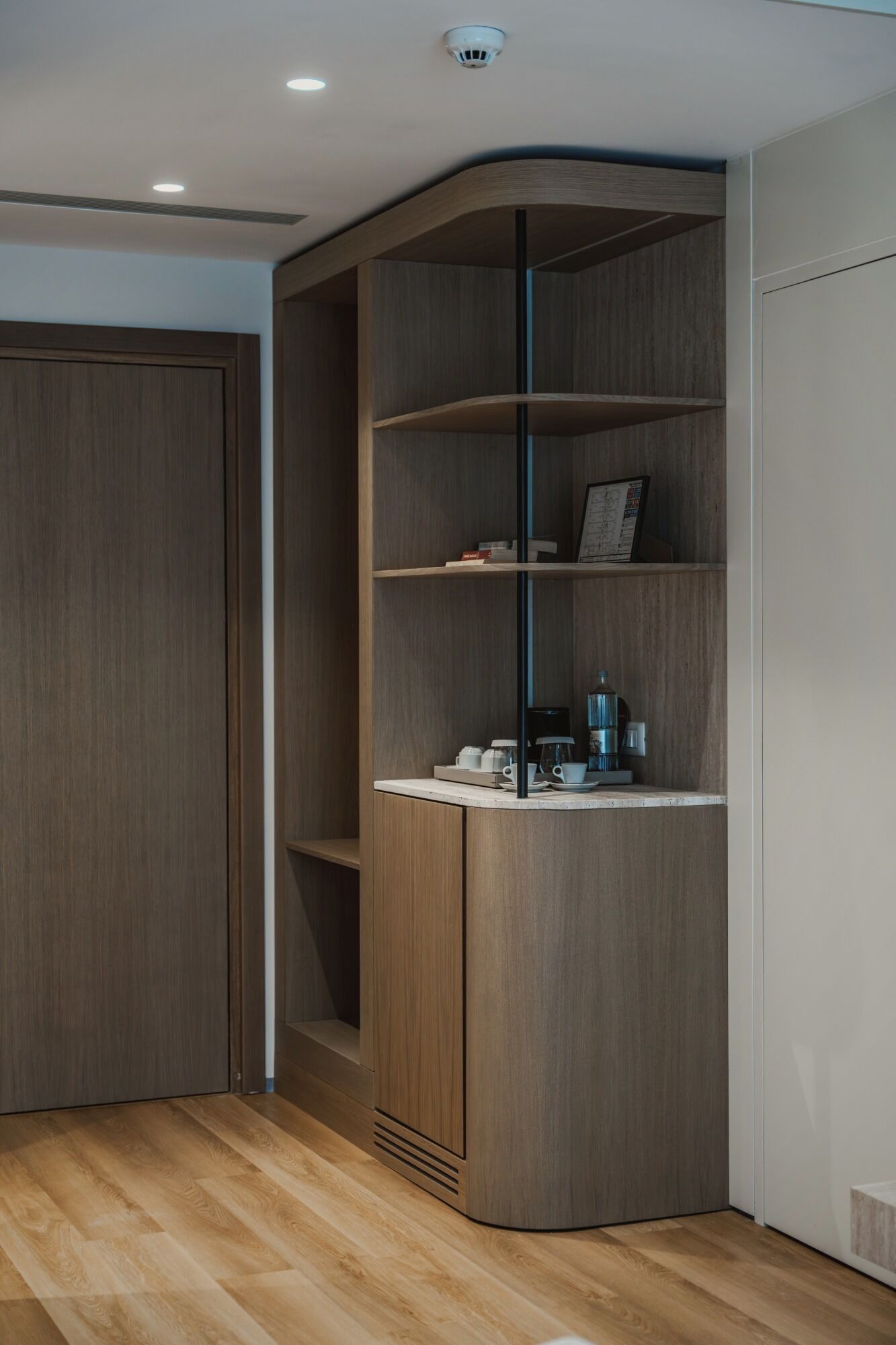 Een hoekhotelkamer met een ingebouwd houten schap, een deur en een koffieapparaat op het aanrecht.