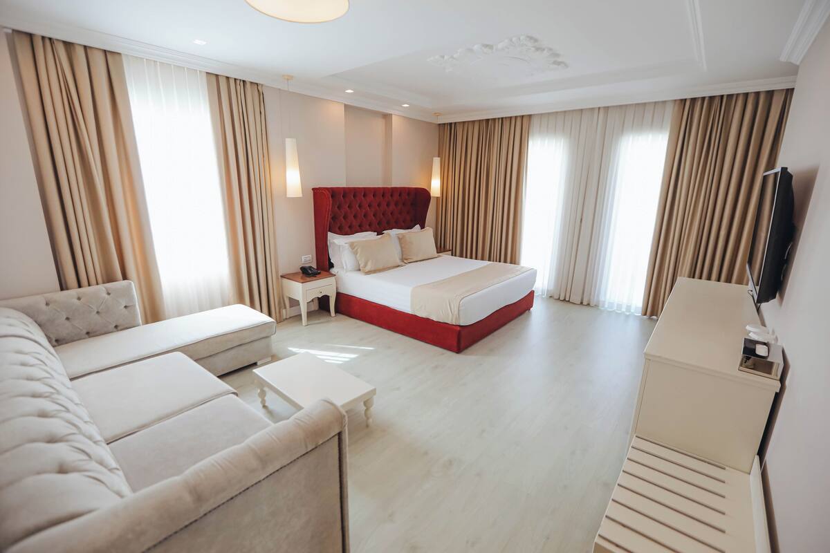 A hotel room with a large bed, a sofa, a nightstand, and a television.