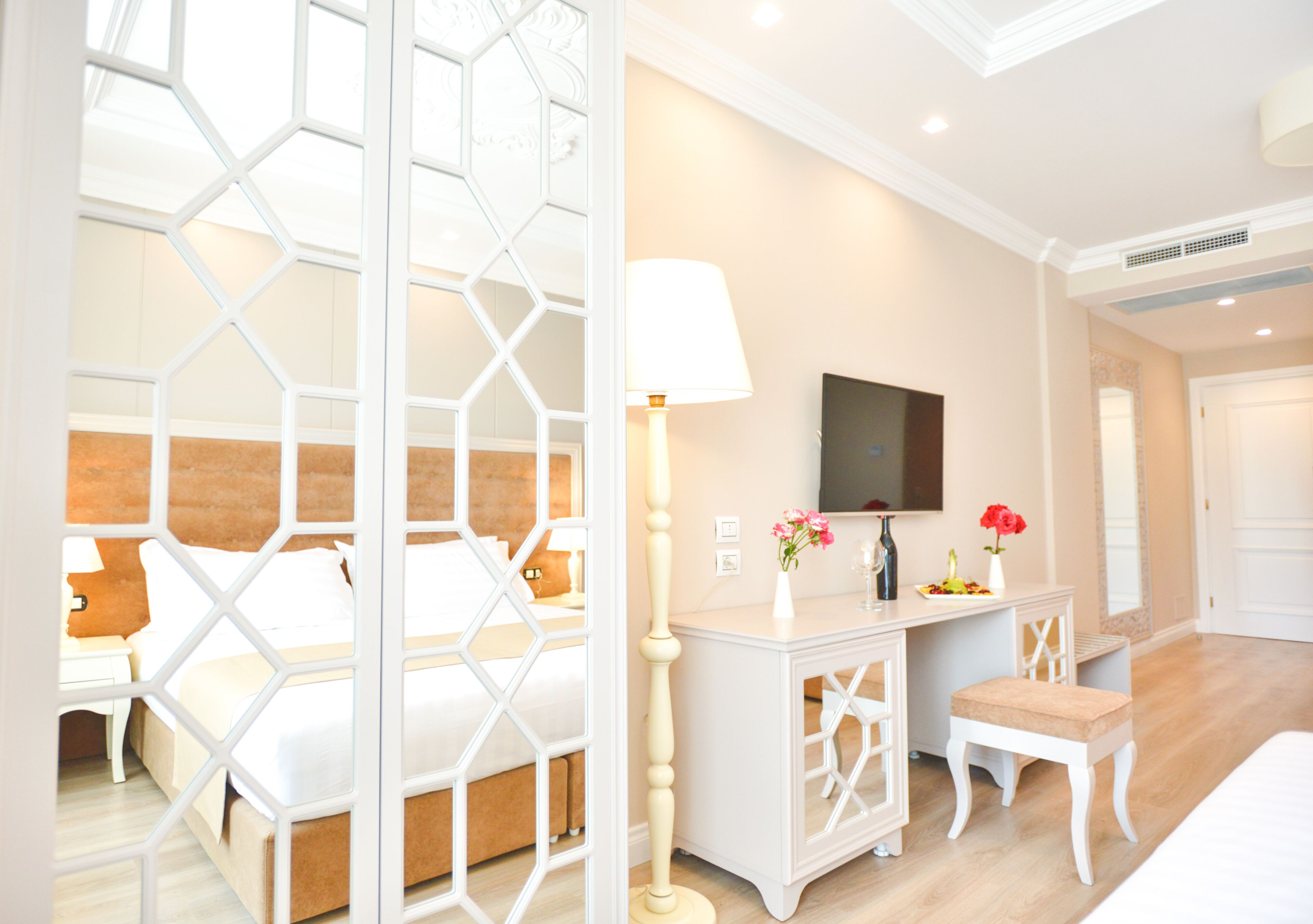 Quarto de hotel com cama, escrivaninha, cadeira, televisão e um separador decorativo.