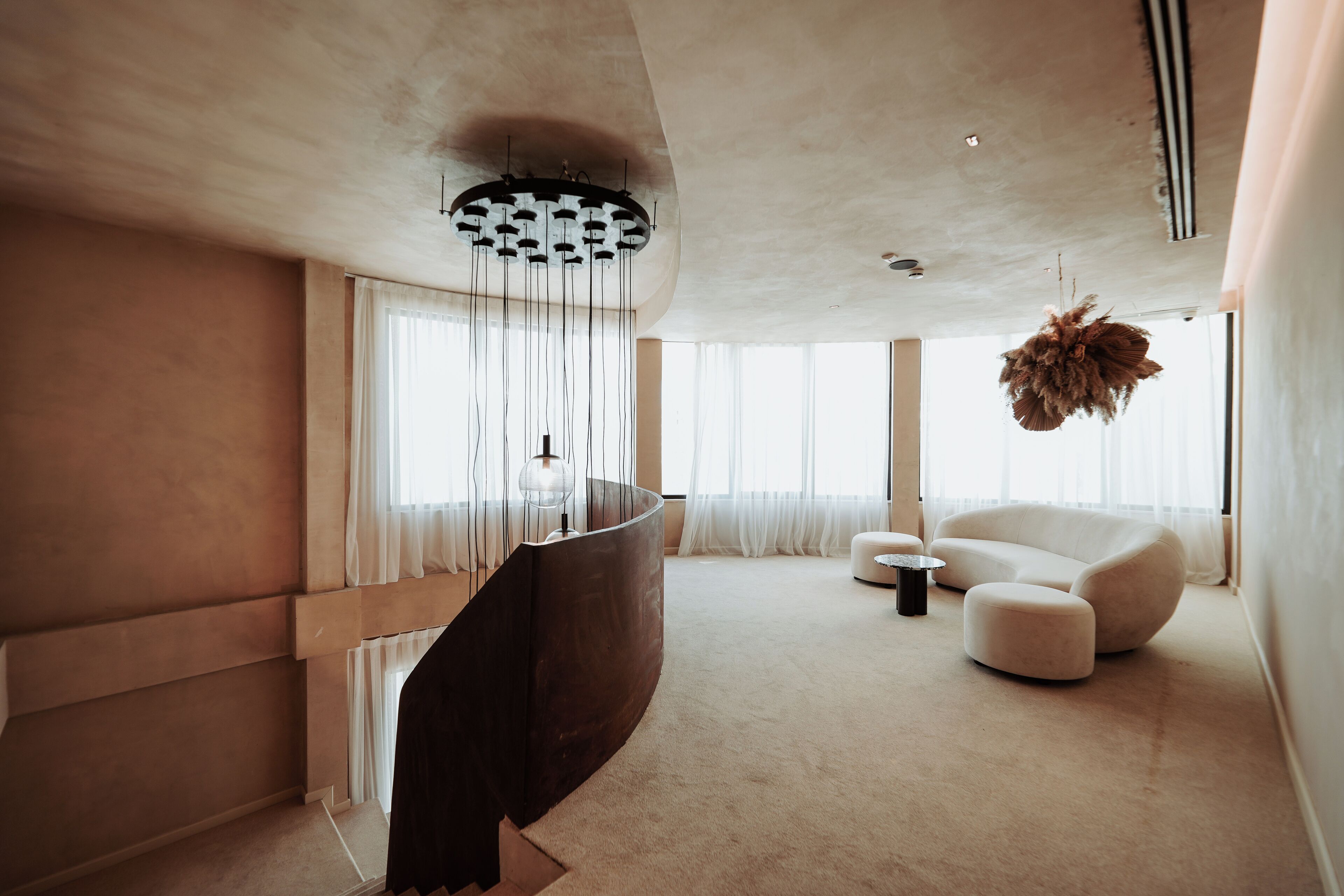 A modern living room with a curved dark wood staircase, a white sofa, and a hanging plant.