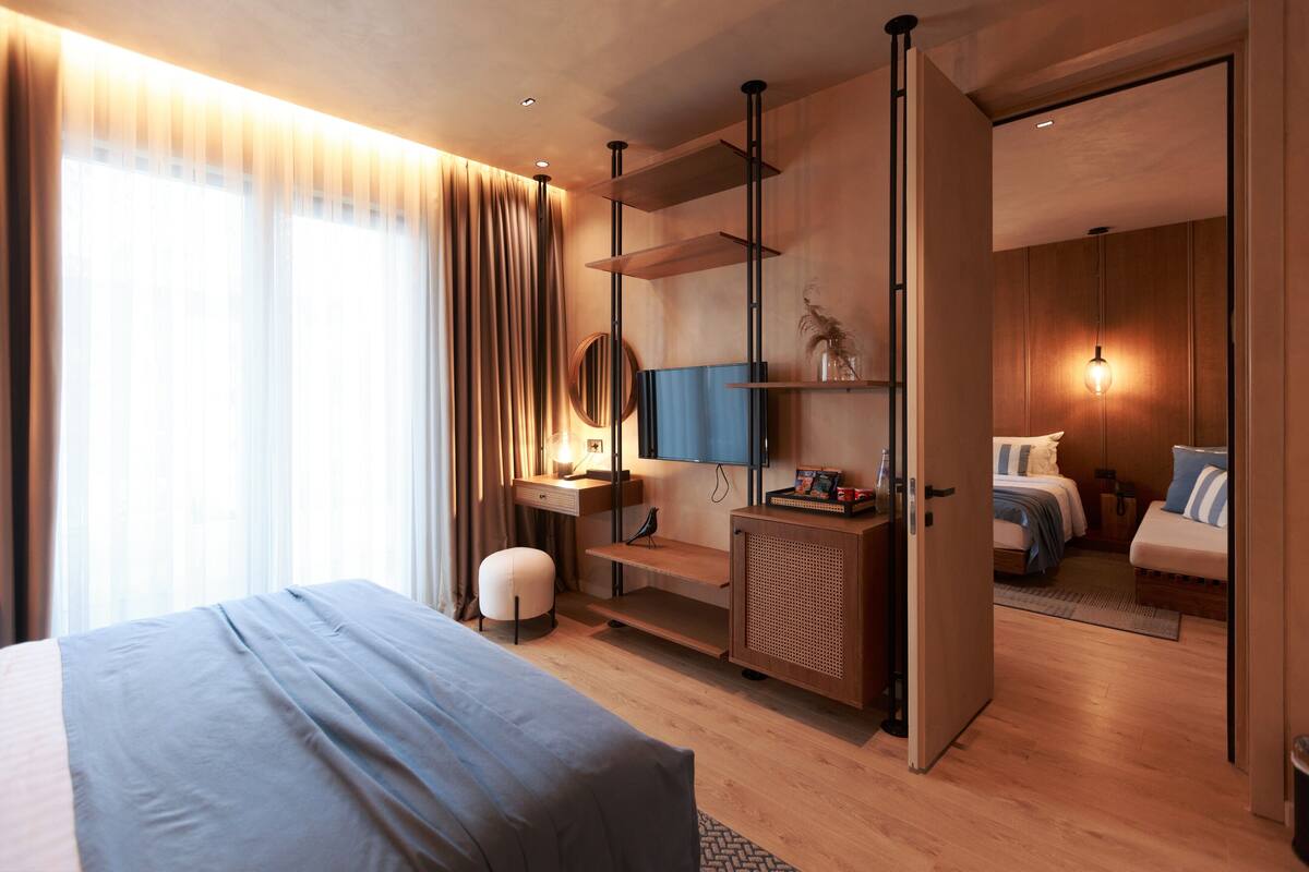 A modern hotel room with a large bed, a desk with a chair, a TV, and a wardrobe.
