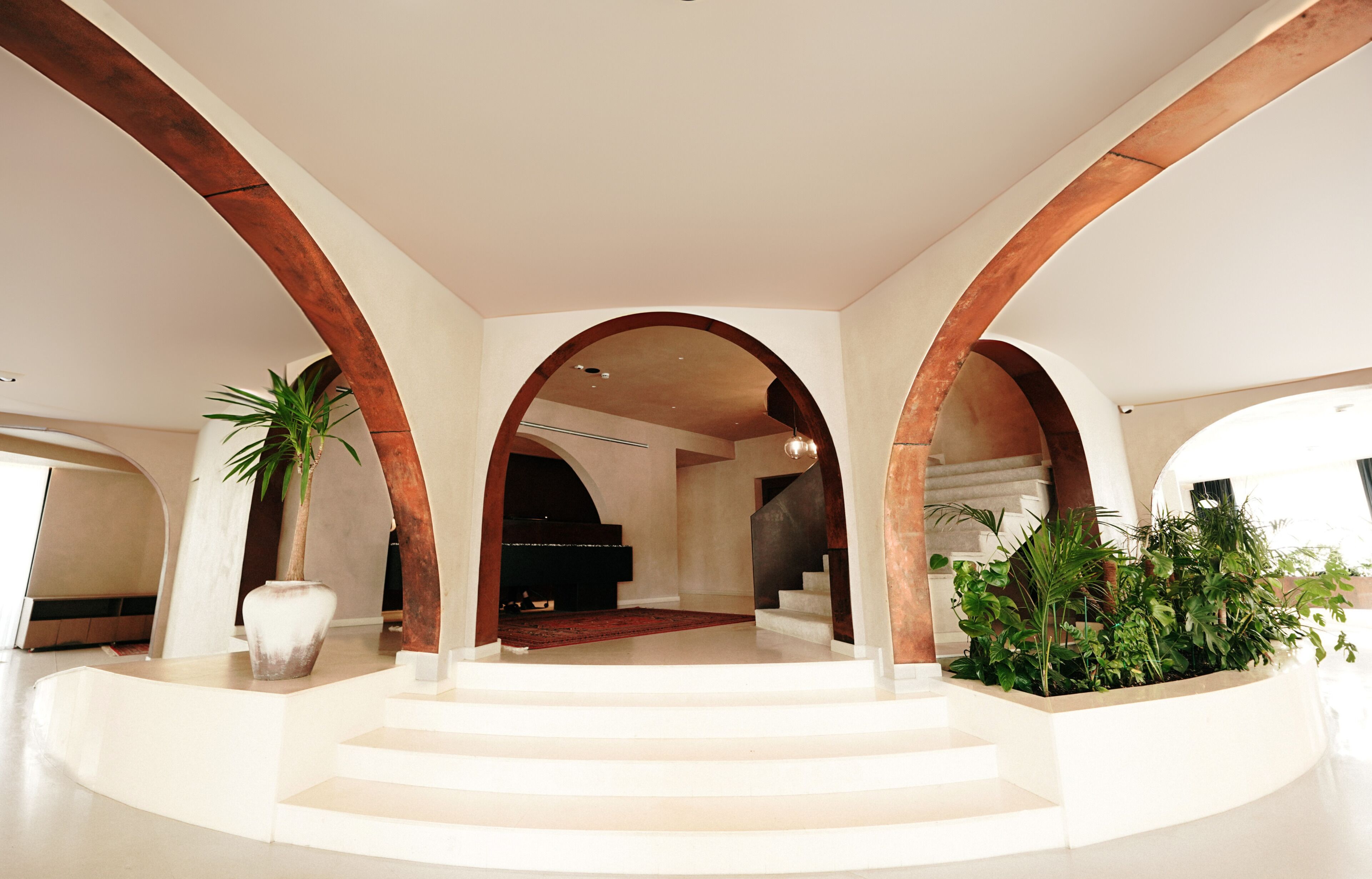 A spacious interior with a grand staircase, arched ceilings, and a piano in the background.