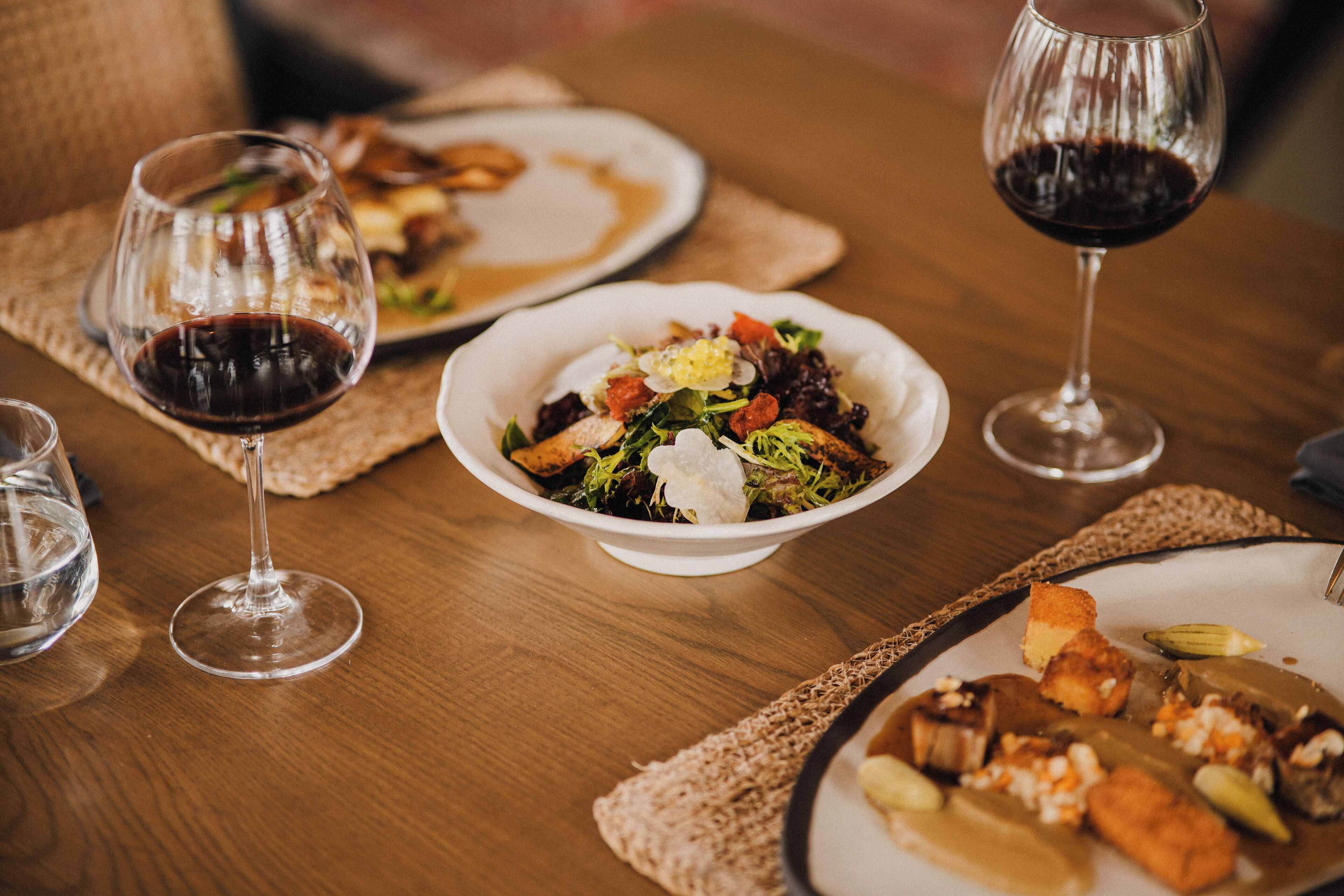 Una mesa de comedor con platos de comida y copas de vino.