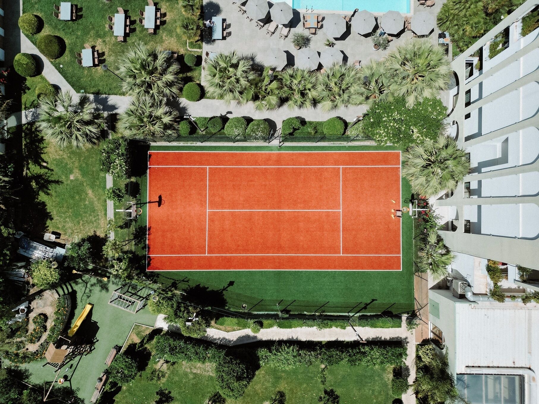 Vue aérienne d’un court de tennis entouré de verdure et d’un espace piscine.