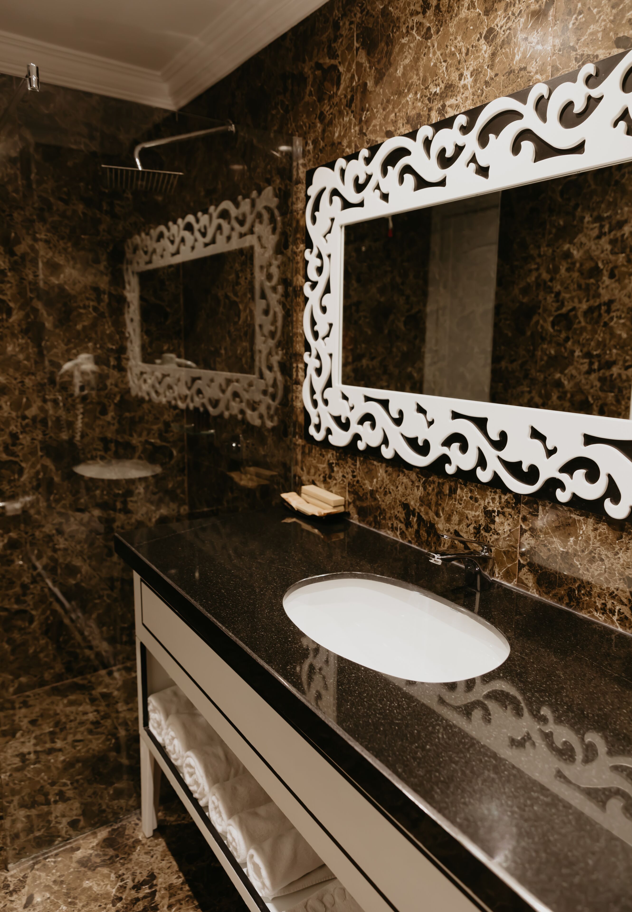 Une salle de bain avec un mur en marbre, un lavabo blanc et un grand miroir doté d’un cadre orné.
