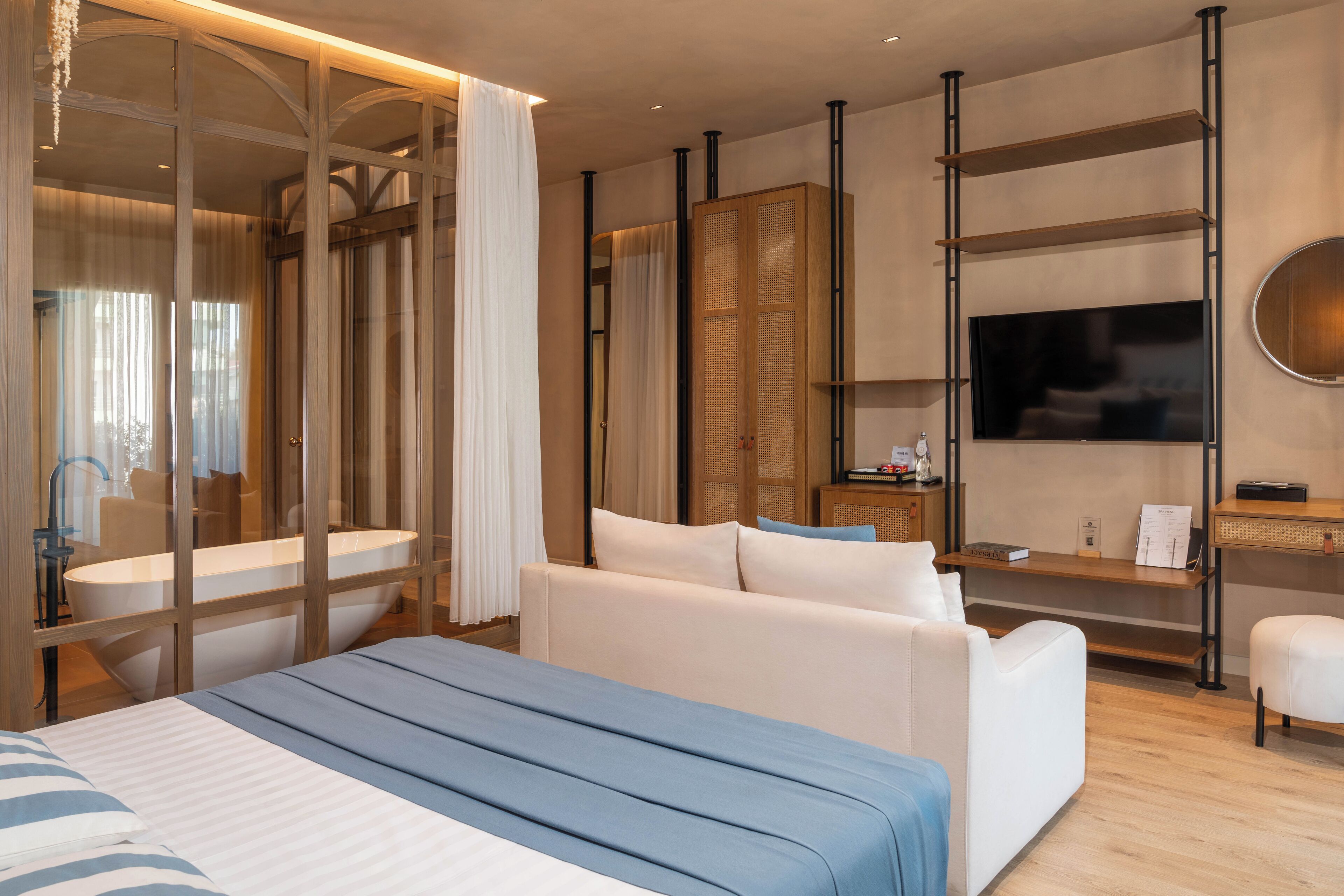 Una habitación de hotel moderna con una cama grande, un sofá, un televisor y un estante de madera.