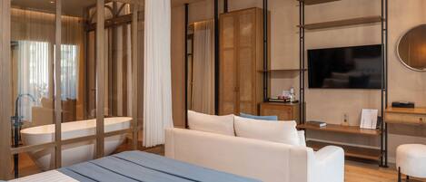 A modern hotel room with a large bed, a sofa, a television, and a wooden shelf.
