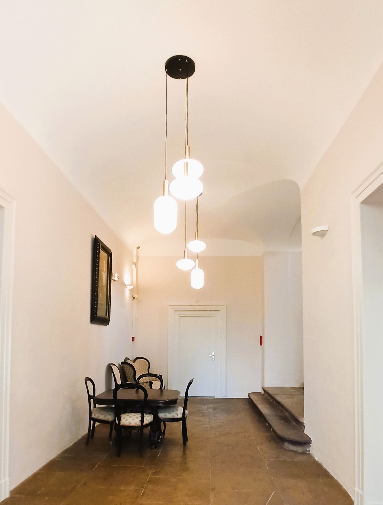 A dining area with a table and chairs, a hanging light fixture, and a staircase leading to another room.