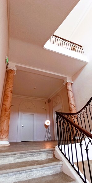 A staircase with marble columns, a black metal railing, and a white door at the top. - Apartment (Conqueyrac)