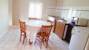A compact kitchen with a dining area, featuring a white tiled backsplash, a built-in oven, and a compact refrigerator. - Apartment (Conqueyrac)