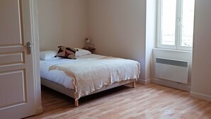A bedroom with a bed, a bedside table, a lamp, and a window. - Apartment (Conqueyrac)