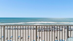 Blick auf einen Strand mit Liegestühlen und Sonnenschirmen, ein Geländer im Vordergrund und das Meer im Hintergrund.