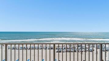A beach view with rows of sun loungers and umbrellas, a railing in the foreground, and the ocean in the background.