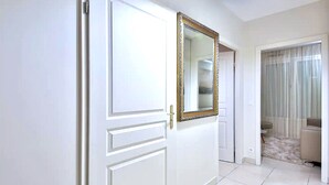 Un corridoio con una porta bianca, uno specchio con cornice dorata e una stanza con un divano beige e una parete in pietra.