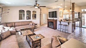 A spacious living room with a large sectional sofa, a fireplace, and a kitchen area with bar stools. - Heated Pool & Game Room: Lake Havasu Retreat (Lake Havasu City)