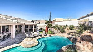 A swimming pool with a curved design, surrounded by lounge chairs and a covered patio area. - Heated Pool & Game Room: Lake Havasu Retreat (Lake Havasu City)