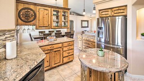 A kitchen with granite countertops, wooden cabinets, a stainless steel refrigerator, and a central island with a potted plant. - Heated Pool & Game Room: Lake Havasu Retreat (Lake Havasu City)