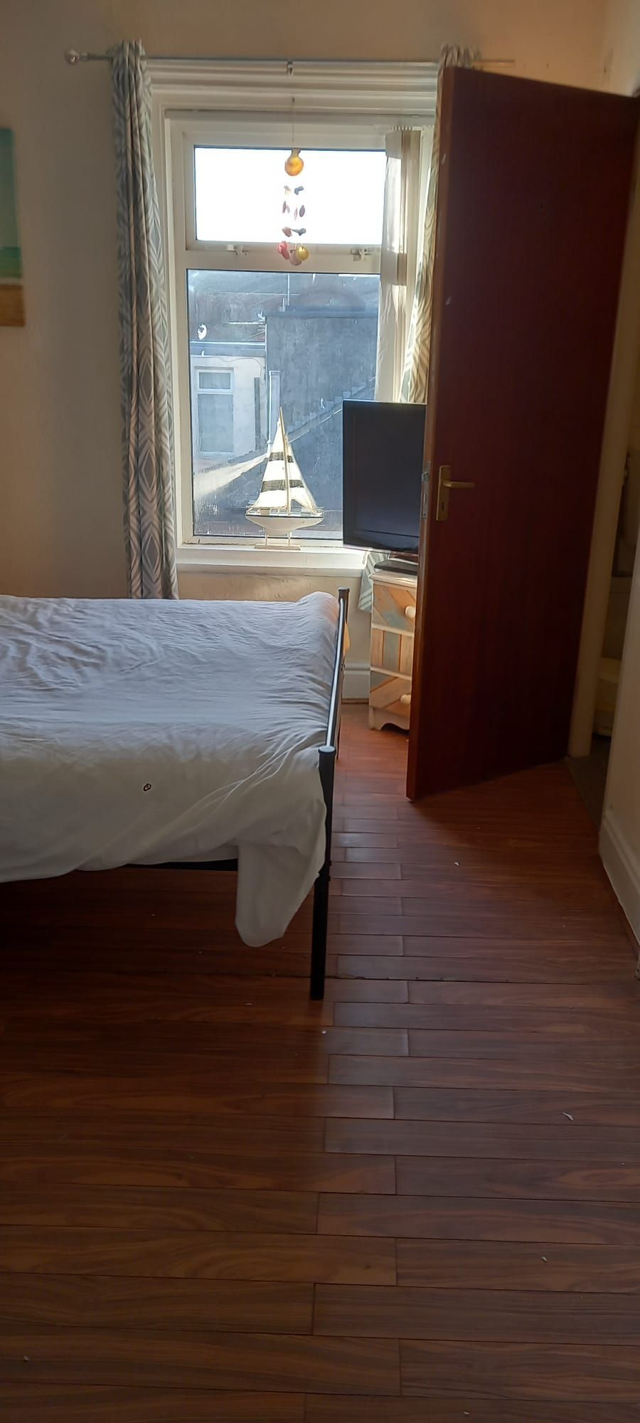 A bedroom with a bed, a TV, and a window with a view of a building and a sailboat.