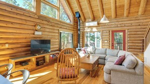 A log cabin interior with a wooden floor, a television, a sofa, a chair, and a staircase. - Walk to Pine Mountain Lake: Spacious Family Cabin (Groveland)