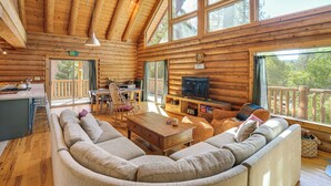 A log cabin interior with a large sofa, dining table, TV, and wooden floors. - Walk to Pine Mountain Lake: Spacious Family Cabin (Groveland)