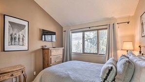 A bedroom with a large bed, a wooden dresser, a TV mounted on the wall, and a window with curtains. - 3BR Riverfront Retreat 1 Min to Vail or BC Shuttle (Eagle-Vail)