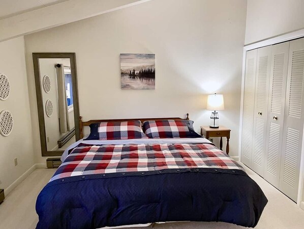 A bedroom with a bed, a nightstand with a lamp, a mirror, and a wardrobe.