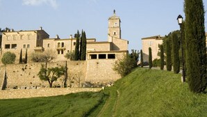 Un edificio storico con una torre imponente, circondato da un muro in pietra e rigogliosa vegetazione.