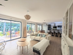 Ein großzügiger Wohnbereich mit einer Couch, einem Couchtisch und einem Esstisch, eine Küche mit Barhocker und große Schiebeglasüren zum Patio.