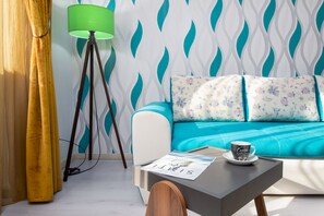 A modern living room with a teal sofa, a green floor lamp, and a coffee table with a magazine and a cup.