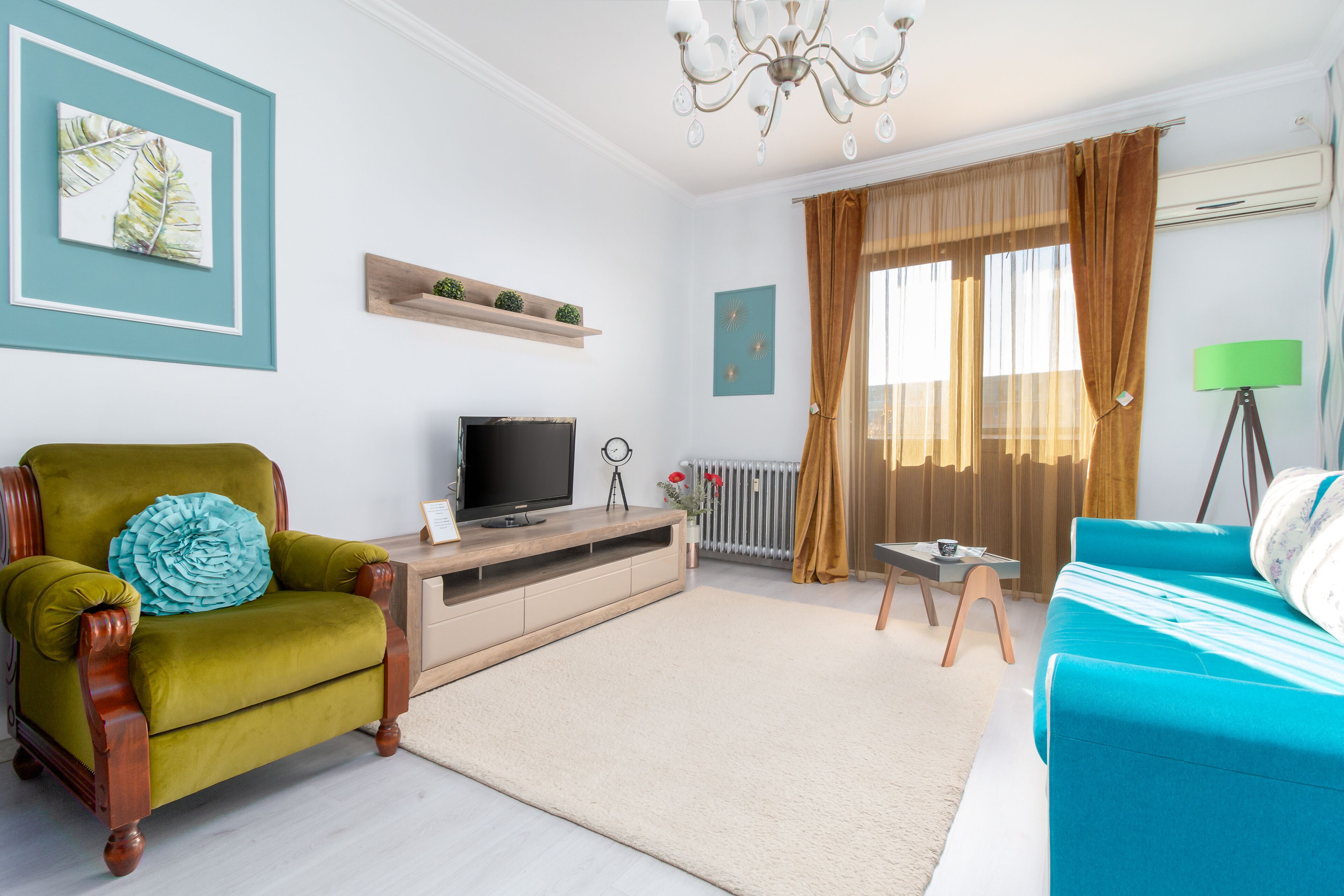 Uma sala de estar com uma poltrona verde, um sofá azul, uma televisão e um radiador.
