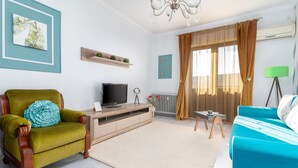 Ein Wohnzimmer mit einem grünen Sessel, einem blauen Sofa, einem Fernseher und einer Heizung.