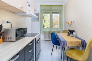 Cozinha compacta com micro-ondas, fogão e pia. Há uma mesa de jantar com cadeiras e um vaso com flores.